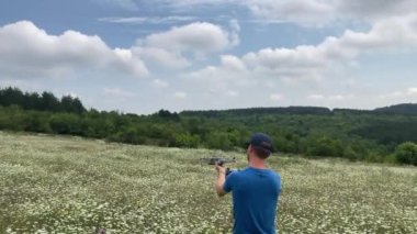 Erkek İHA pilotu uzaktan kumandalı bir cep telefonu ile arka planda orman bulunan güzel bir kır çiçeği çayırına insansız hava aracı fırlatıyor - Nr Veliko Tarnovo, Bulgaristan