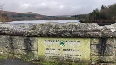 Arka planda Dartmoor Ulusal Parkı 'nın muhteşem bataklığı ve gölü olan Viktorya Burrator Reservoir için bir anıt taşı. Kışın bulutlu bir günde Nr Yelverton, Devon, İngiltere