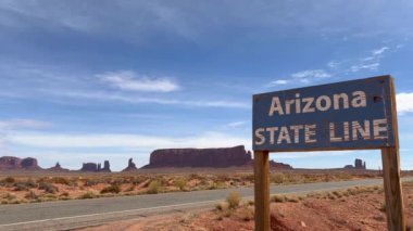Arizona eyalet sınırındaki ilkel ahşap tabela Navajo Ulusal Arazisi 'nin kenarında güzel kumtaşı izmaritleri ve arka planda boş bir yol ile Arizona, ABD
