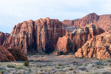 Kar Kanyonu Parkı 'ndaki yüksek kırmızı Navajo kumtaşı kayalıkları. Alttaki otlak vadiden nefes kesen kaya oluşumları dik bir şekilde yükseliyor. Sabahın erken saatlerinde çekildi - St George, Utah, ABD