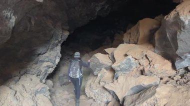 Bir kadın, volkanik kayalarla çevrili siyah bir lambayla siyah bir lav tüneline giriyor. Kar Kanyonu Eyalet Parkı, St George, Utah, ABD