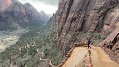 Bir kadın yürüyüşçü, Zion Ulusal Parkı 'ndaki Batı Halka Yolu' nda aşağıdaki kanyonun çarpıcı manzarasıyla birlikte yürür. Bu yol ünlü Melekler Şehri Utah, ABD 'ye çıkıyor.