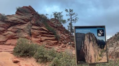 Utah, Zion Ulusal Parkı 'ndaki ünlü Melekler İniş Yürüyüşü için uyarı işareti. İşaret yürüyüşçülere, arka plandaki yürüyüşün başlamasıyla birlikte yolun tehlikeleri hakkında tavsiyede bulunuyor - ABD