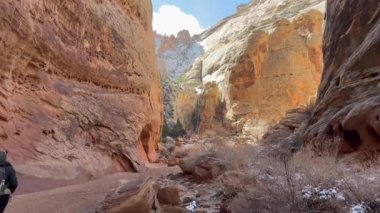 Bir kadın yerde karla kaplı Grand Wash olarak bilinen muhteşem bir çöl kanyonunda yürüyüş yapıyor. Utah, Capitol Resif Ulusal Parkı 'ndaki güneşli günün ve güzel manzaranın tadını çıkarıyor.