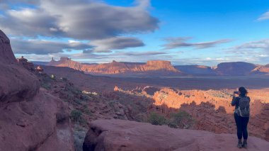 Bir kadın Moab, Utah yakınlarındaki çölde yürürken inanılmaz manzaranın tadını çıkarıyor. Sabahın erken saatlerinde güzel kızıl kaya oluşumlarının fotoğraflarını çekmek için duruyor.