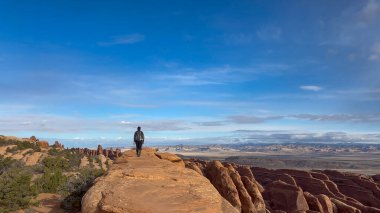 Yüksek, dar bir kum taşı yüzgeci formasyonunda, çöl manzaralı bir kadın yürüyüşçünün geniş açılı görüntüsü. Utah, Arches Ulusal Parkı 'ndaki Devils Garden Trail' de çekildi.