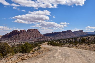 Utah 'taki Capitol Resifi Ulusal Parkı' nın manzarasında muhteşem Waterpocket Katları dağınık bulutlarla mavi bir gökyüzünün altında. Bu virajlı toprak yol Burr Yolu olarak bilinir.