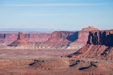 Utah, Canyonlands Ulusal Parkı 'ndaki ikonik Grand View Point' ten çarpıcı panoramik manzara. Fotoğraf görkemli kırmızı kaya oluşumlarını ve mavi gökyüzü altında batı manzarasını yakalar.