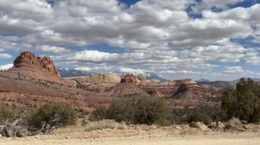 Utah 'taki Capitol Reef Ulusal Parkı' ndaki Waterpocket Katliamı 'nın görüntüsü. Kızıl kaya oluşumları, karla kaplı dağlarla birlikte mavi gökyüzünün altında bulutlarla birlikte. Burr Trail Road - ABD