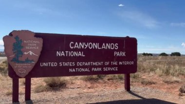 Moab, Utah, ABD - 03.06.2024: Gök Bölgesi 'ndeki ada için Canyonlands Ulusal Parkı giriş işareti. İşaret beyaz harflerle kahverengi, gökyüzü birkaç beyaz bulutla mavi..