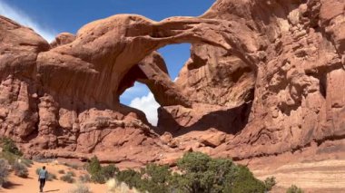 Kadın yürüyüşçü, Arches Ulusal Parkı 'ndaki görkemli Double Arch kaya oluşumuna doğru bir çöl yolunda yürüyor. Derin mavi gökyüzü, Utah 'ın kırmızı kayalarıyla mükemmel bir tezat oluşturuyor.