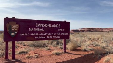 Moab, Utah, ABD - 03.10.2024: Utah 'taki Needles ilçesi için Canyonlands Ulusal Parkı tabelasının statik çekimi. Kanyonlar ve çölün ikonik kırmızı kayaları arka planda görünür..