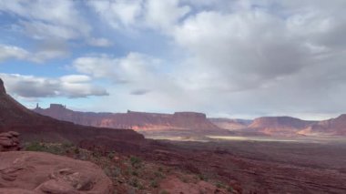 Parçalı bulutlu bir sabahta Utah, Moab yakınlarındaki Fisher Kuleleri 'nin etrafındaki güzel manzaraya bakan yavaş çekim videosu. Kızıl kaya oluşumları çöle karşı göze çarpıyor.