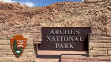 Moab, Utah, ABD - 03.07.2024: Utah 'taki Arches Ulusal Parkı' nın giriş levhasını kapatın. Simgesel kahverengi tabela, arka planda kum taşı dağları olan ziyaretçileri karşılıyor..