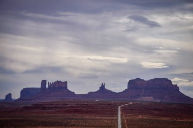 A hazy day over the iconic Monument Valley formations from Forrest Gump Point in Utah. The long road stretches into the distance, surrounded by stunning rock formations under a dramatic sky - USA clipart