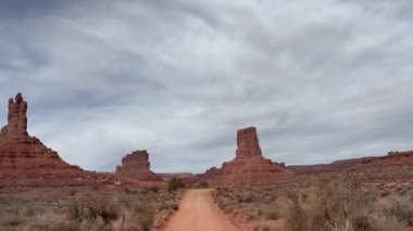 Bakış açısı POV sürüşü Utah, ABD 'deki Tanrılar Vadisi' nde gerçekleşti. Kızıl kaya butte oluşumları, çöl bitkileri ve bulutlu gökyüzü bu off-road macerasında manzaralı batı manzarası boyunca.