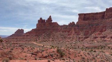 Utah, Tanrılar Vadisi 'ndeki ikonik kırmızı kaya butte oluşumlarının ve çöl manzarasının bir görüntüsü. Bölgeden geçen toprak yol, ABD 'deki kaya oluşumlarının yanından geçerken görülebilir.