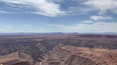 Arka planda Tanrıların Vadisi olan Utahlar 'ın muazzam kanyonlarının güzel, statik bir görüntüsü. Kırmızı kaya oluşumları ve kanyonları, beyaz, tüylü bulutlarla dolu açık mavi bir gökyüzünün altındaki araziyi doldurur.