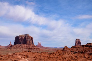 Arizona 'daki John Ford Point Anıt Vadisi' nde görkemli kaya oluşumları. Bu manzarada ikonik kırmızı kaya birikimleri ve parlak mavi gökyüzü altında dağınık bulutlar - ABD