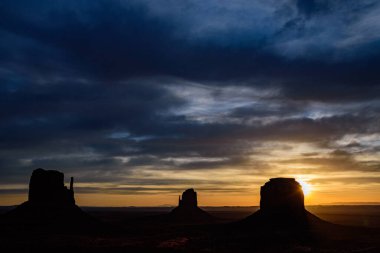 Monument Vadisi 'nde büyüleyici bir gün doğumu, ikonik Mittens ve Merrick Butte' un silüeti. Lens ışığı, Arizona, ABD 'nin güzelliğini vurgulayarak sabah gökyüzüne çarpıcı bir dokunuş ekliyor..