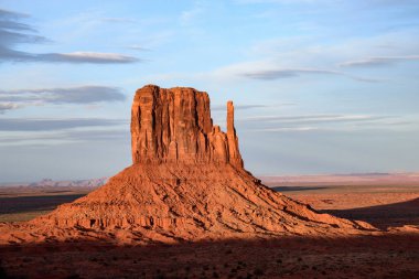 Arizona, Anıt Vadisi 'ndeki ikonik Batı Mitten Butte manzarası muhteşem bir günbatımının sıcaklığıyla aydınlanıyor. Güneybatının eşsiz jeolojik oluşumlarını gösteren bir manzara..
