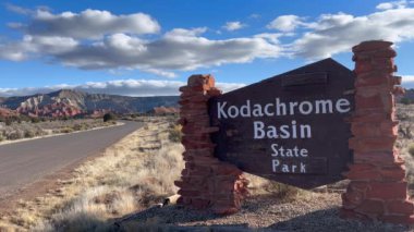 Utah, ABD 'deki Kodachrome Havzası Eyalet Parkı' nın giriş tabelasının manzarası. İşaret ahşap ve taştan yapılmıştır ve çarpıcı çöl manzarası ve park yolu ile çevrilidir.. 