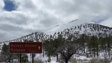 Parçalı bulutlu bir günde karla kaplı Sunset Krateri Ulusal Anıtı. Ön planda bir işaret var. Volkan Arizona, ABD 'de Flagstaff' ın kuzeyinde bulunan bir kül konisidir.