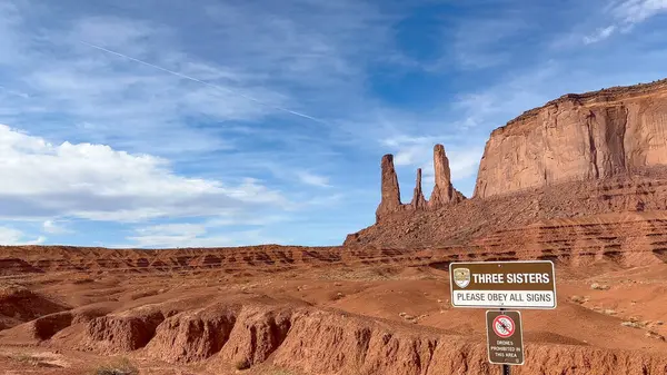 Arizona, Anıt Vadisi 'ndeki Üç Kız Kardeş kaya oluşumlarının inanılmaz manzarası. Amerika 'nın batısının ikonik kırmızı kaya manzarasının manzarası. Öndeki tabelada 