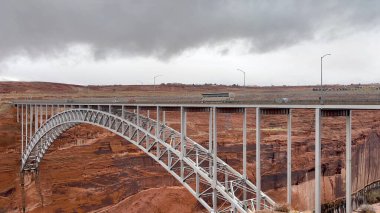 The historic Navajo Bridge in Arizona. Cars and a tour bus drive high over the Colorado River at Marble Canyon as storm clouds gather in the distance - USA clipart