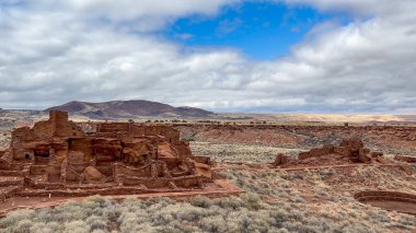 Wupatki Ulusal Anıtı, Arizona 'daki antik Wupatki Pueblo kalıntılarının panoramik manzarası. Kırmızı kumtaşı yapılar, bulutlu mavi gökyüzü ve engin çöl manzarası ABD 'nin tam zıttı.