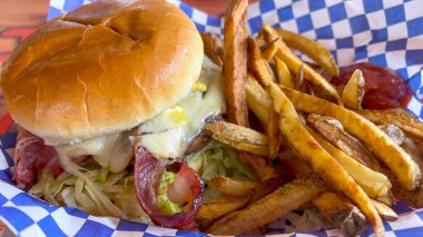 Lezzetli pastırmalı cheeseburger ve yanında kızarmış patates. Hamburger sulu ve eritilmiş peynir, kıtır pastırma ve taze marulla kaplı. Klasik bir Amerikan lokantası - ABD