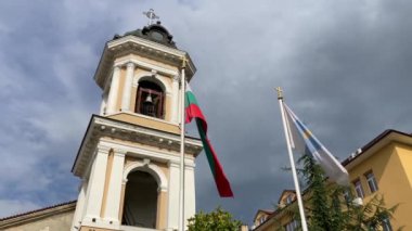 Bulgaristan 'ın Filibe kentinde Sveta Bogoroditsa Kilisesi önünde Bulgar ve Filibe bayrakları dalgalanıyor. Bulutlu bir gökyüzü dramatik bir zemin sağlar.