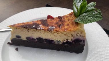 Lezzetli dilimlenmiş yaban mersinli cheesecake Çikolata kabuklu, üstüne taze nane şekeri ve pudra şekeri konmuş.