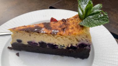 Lezzetli dilimlenmiş yaban mersinli cheesecake Çikolata kabuklu, üstüne taze nane şekeri ve pudra şekeri konmuş.