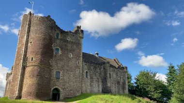 Doune, İskoçya, İngiltere - 07.09.2023: Mavi gökyüzü ve tüylü beyaz bulutlarla güzel bir yaz gününde İskoçya 'daki Doune Kalesi. İskoç bayrağı şatonun tepesinde gururla dalgalanıyor..