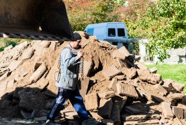 Eski taş bloklar ve kazıcı kovasının önündeki inşaat alanında çalışan bir adam. Ukrayna, Zhytomyr, 12 Ekim 2022