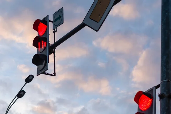 Traffic light with red signal against background of clouds at sunset