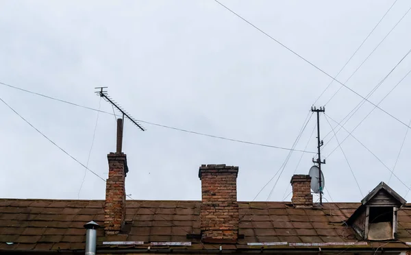 灰色天空背景下带有砖制烟囱和电线的老房子屋顶 — 图库照片