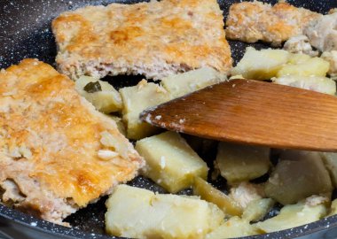 Pieces of meat pie and potatoes with wooden spoon in frying pan close-up