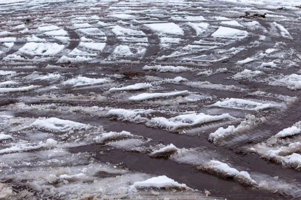 Messy tracks of car tires on melting snow on asphalt of the road