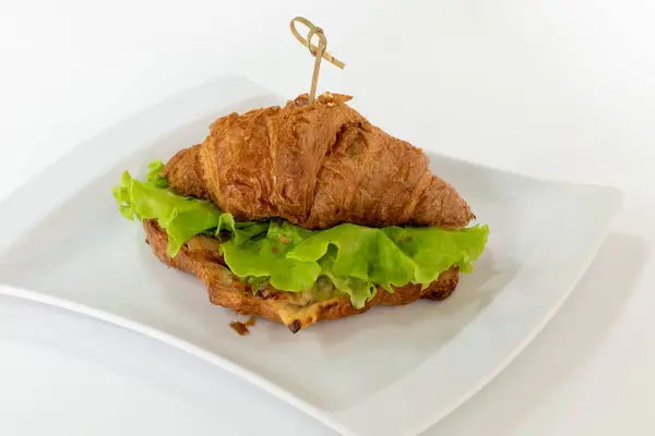 Appetizing croissant with meat, sauce and salad on white plate on white background