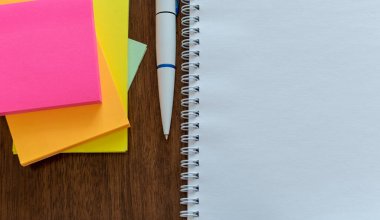 Çok renkli kağıt çıkartmaları, tükenmez kalem ve tahta masaya yakın duran beyaz günlük sayfası. Üst görünüm