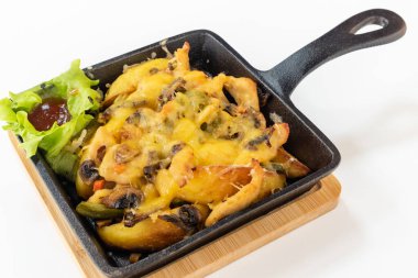 Erimiş peynirin altında patates ve mantarlı fırınlanmış et, salata ve sos beyaz arka planda tahta tahtada metal tavada.