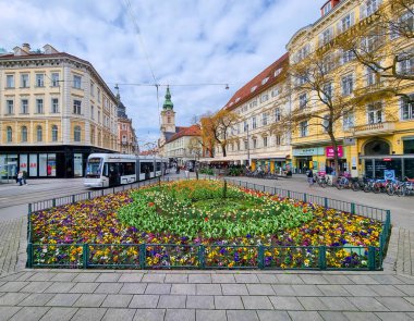 Graz, Avusturya - 26.03.2023: Jakominiplatz Meydanı 'ndaki renkli bahar çiçekleri ve arka planda Parish Kilisesi, Avusturya' nın Steiermark bölgesindeki Graz kentindeki ünlü eğlence merkezi. 