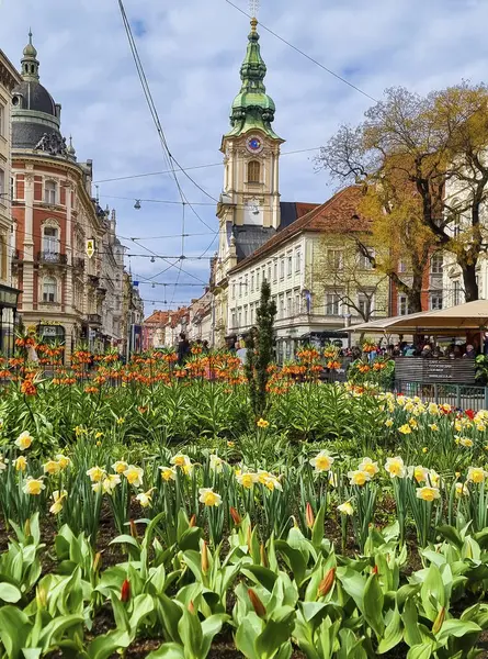 グラーツ オーストリア 2023 バックグラウンドのジャキミンピプラッツ広場と教区教会のカラフルな春の花 グラーツの街で有名なアトラクション ステアマーク地域 オーストリア ストック写真