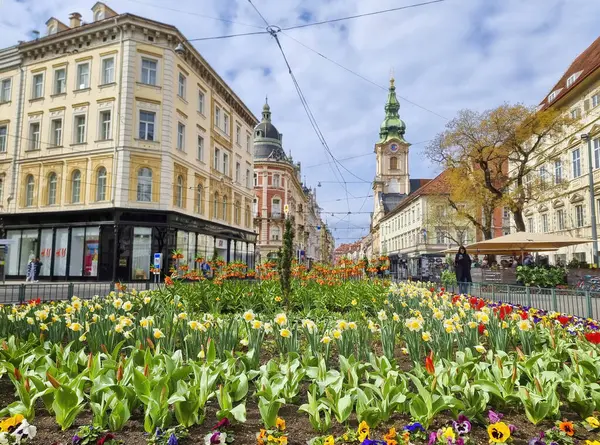 グラーツ オーストリア 2023 バックグラウンドのジャキミンピプラッツ広場と教区教会のカラフルな春の花 グラーツの街で有名なアトラクション ステアマーク地域 オーストリア ロイヤリティフリーのストック画像