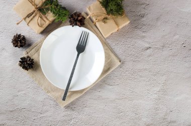 Noel sofrası. Boş beyaz tabak, çatal bıçak takımı ve el sanatları kağıdıyla ışıklandırma masasında hediyeler. Olay tablosu dekorasyonu. 