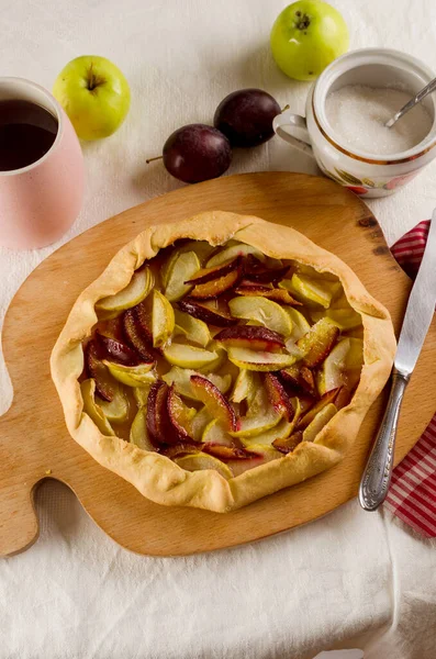 Homemade galette with apple and plum on a white linen tablecloth. Open pie. Top view of homemade pie crust on the table. rustic home baked fruit pie.