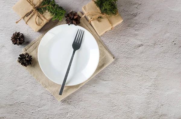 Noel sofrası. Boş beyaz tabak, çatal bıçak takımı ve el sanatları kağıdıyla ışıklandırma masasında hediyeler. Olay tablosu dekorasyonu. 