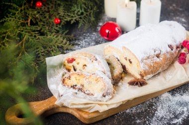 Koyu ahşap masada, ksenli ağaç dalları ve süslemeleri olan kraft kağıdının üzerinde çalınmış. Yılbaşı Alman geleneksel meyveli ekmeği kurutulmuş böğürtlen, fındık ve pudra şekeriyle çalındı.. 